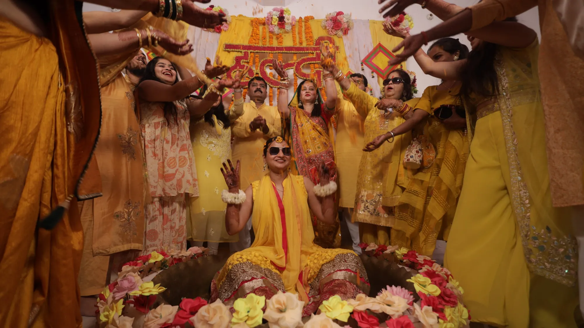 Bride at her haldi ceremony as family showers her with flowers