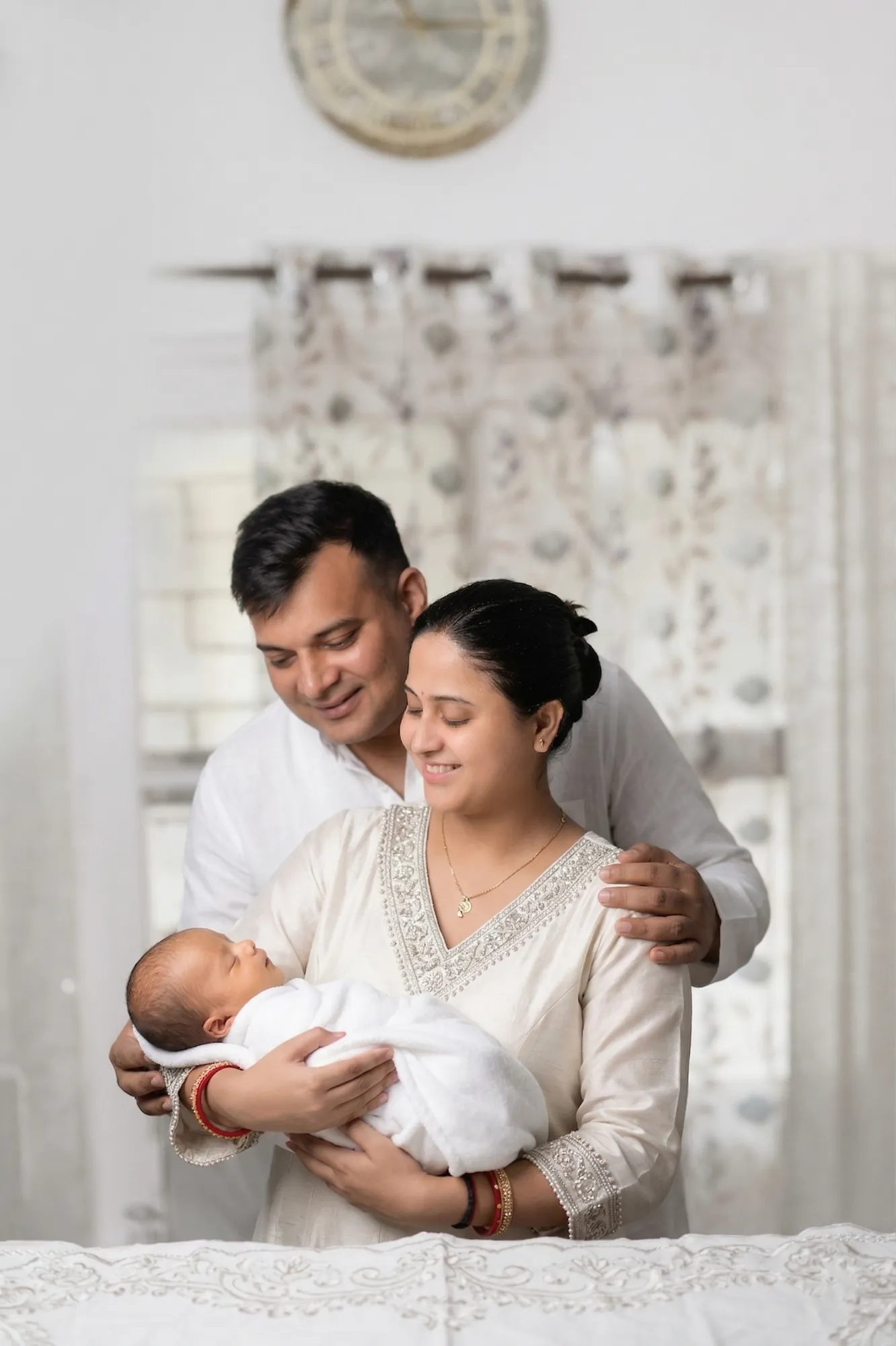 New parents in white holding their newborn